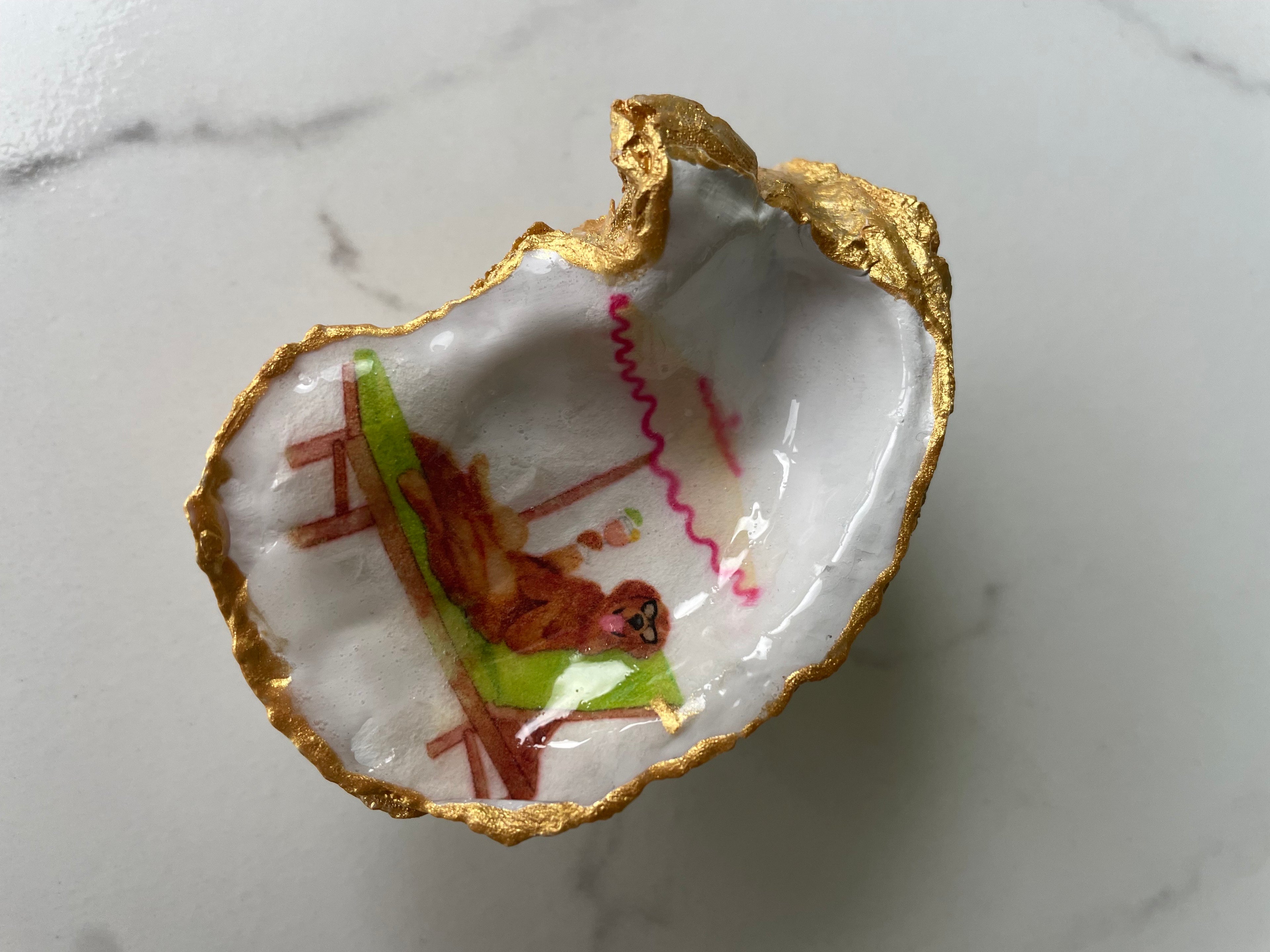 Hero shot of Labrador Paradise gilded oyster shell ring dish with gold paint edging, displayed on a gold stand