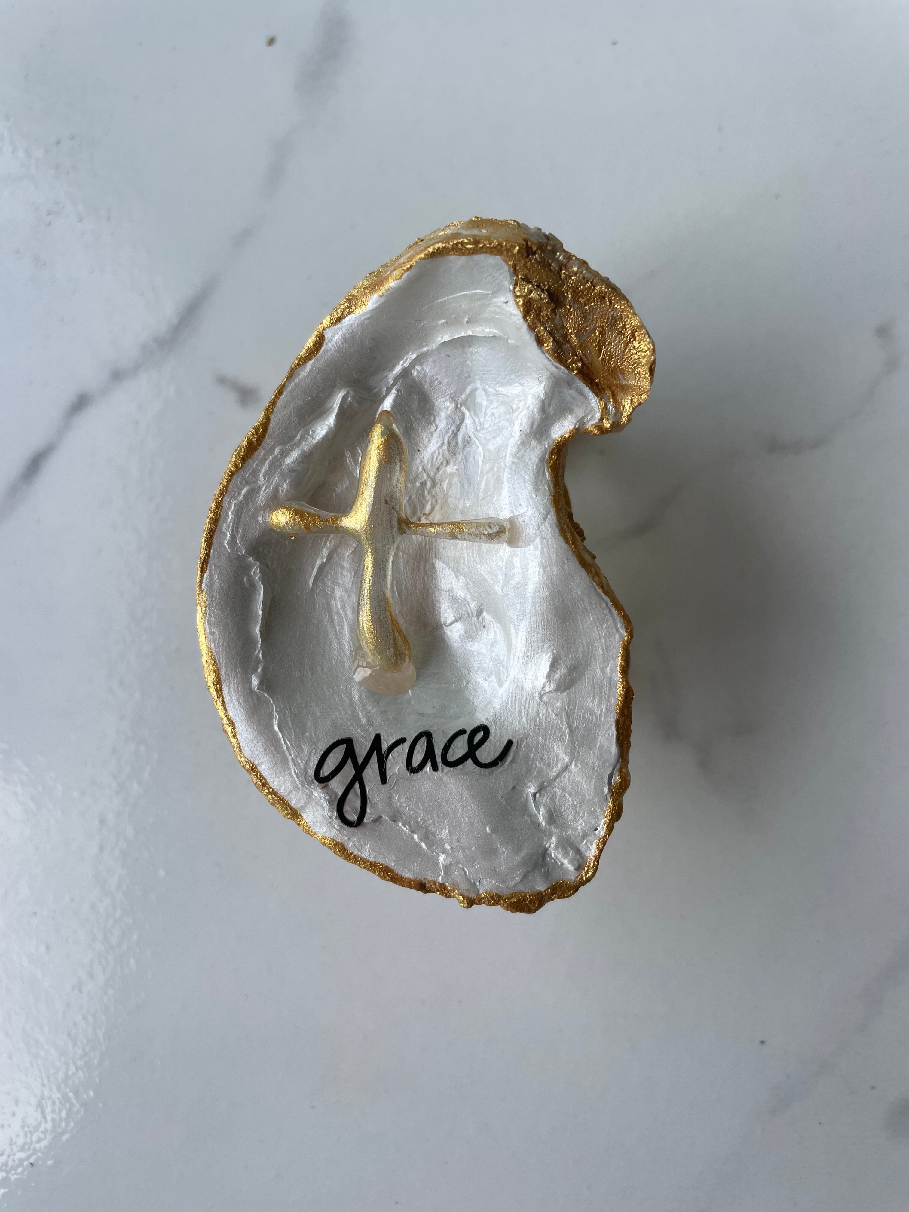 "Grace" Inspiration Series gilded oyster shell trinket dish on gold stand — hand-applied typographic lettering with dimensional gold cross accent, handmade by The Golden Shoreline