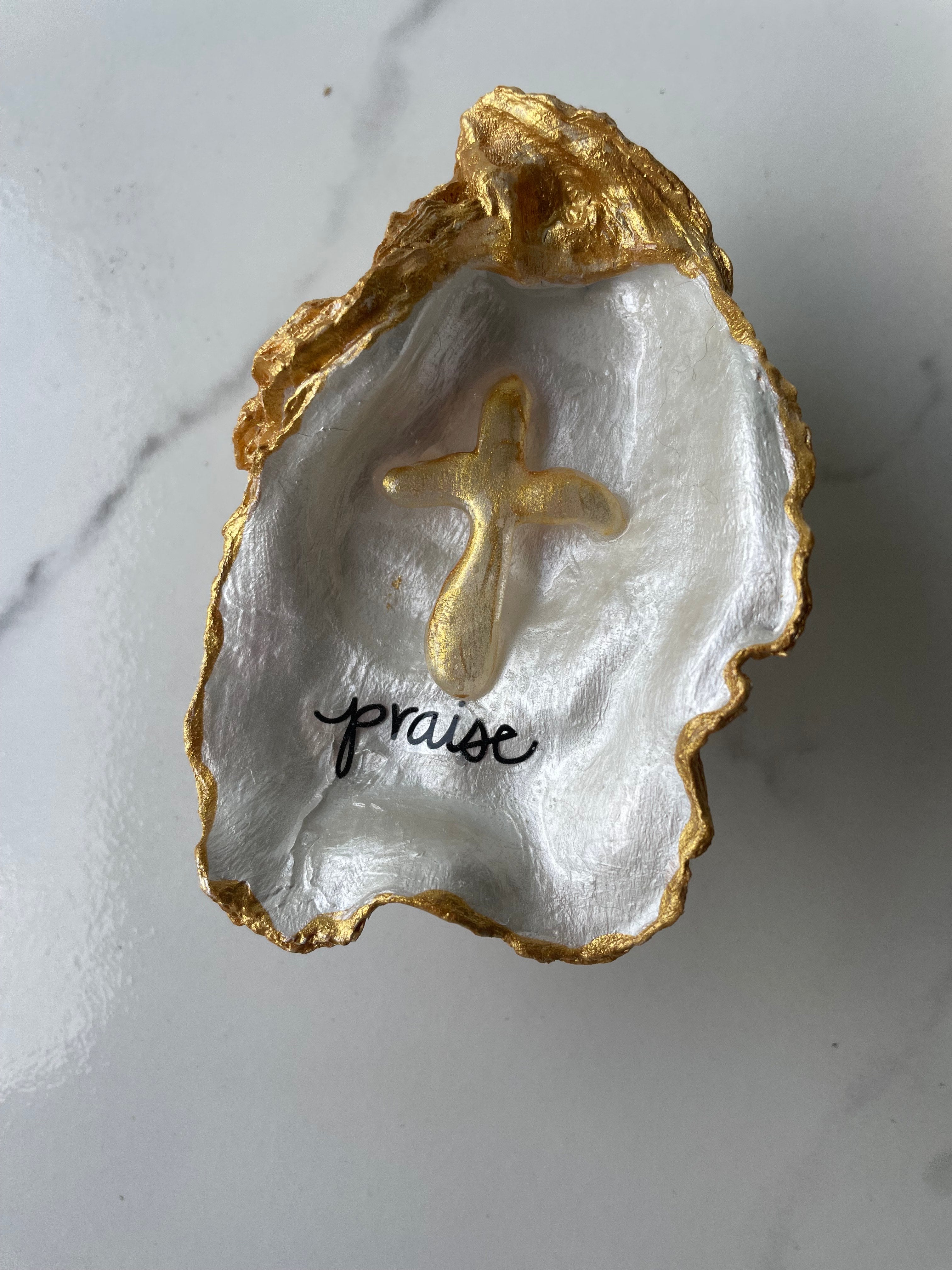 "Praise" Inspiration Series gilded oyster shell trinket dish on gold stand — hand-applied typographic lettering with dimensional gold cross accent, handmade by The Golden Shoreline