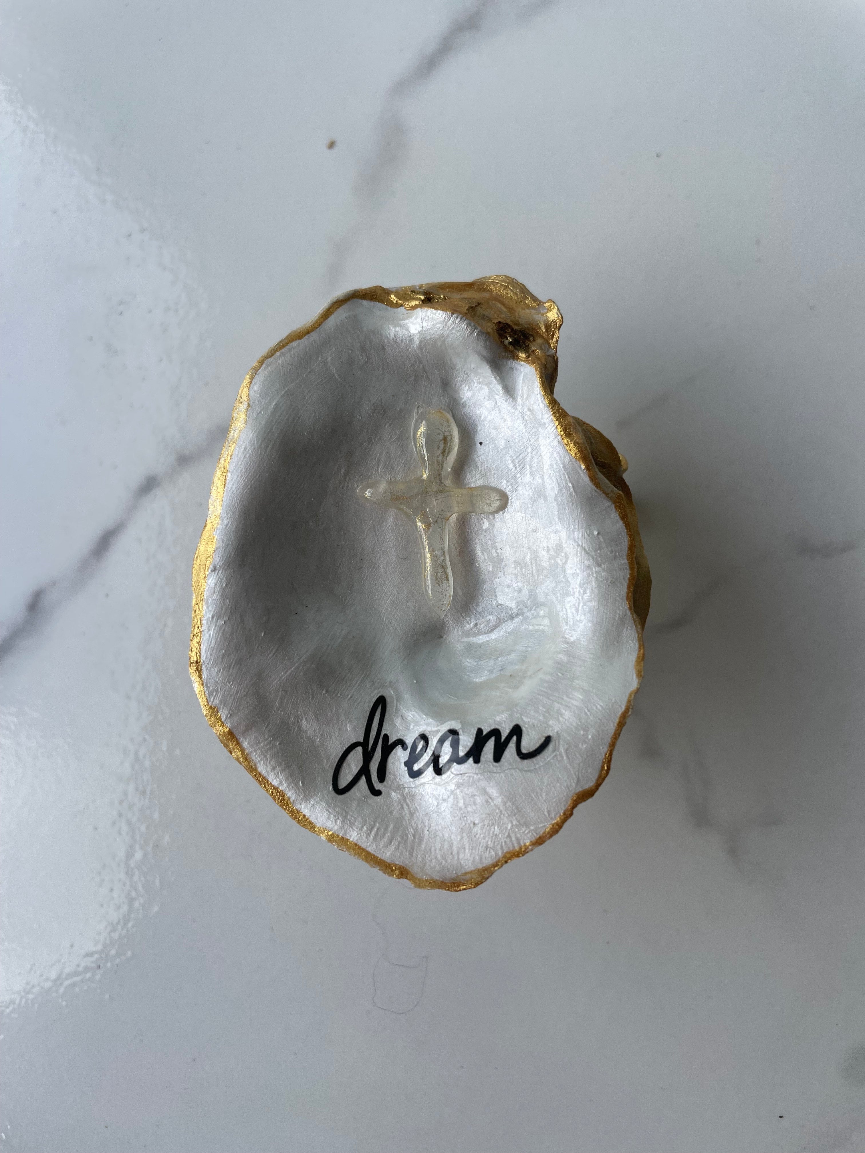 "Dream" Inspiration Series gilded oyster shell trinket dish on gold stand — hand-applied typographic lettering with dimensional gold cross accent, handmade by The Golden Shoreline