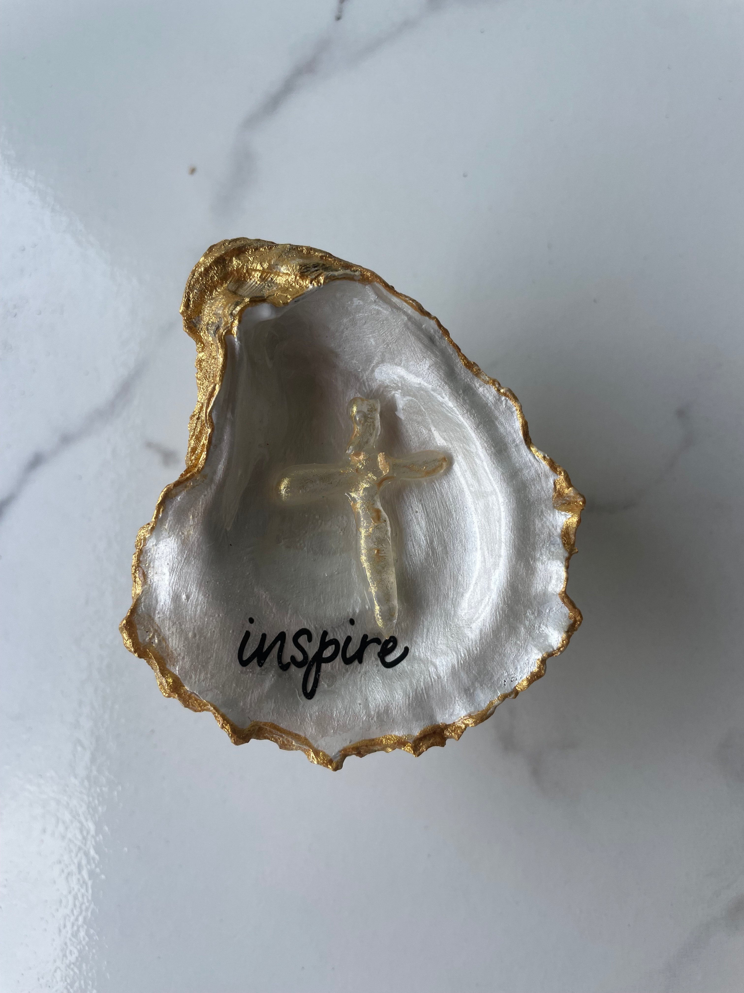 "Inspire" Inspiration Series gilded oyster shell trinket dish on gold stand — hand-applied typographic lettering with dimensional gold cross accent, handmade by The Golden Shoreline