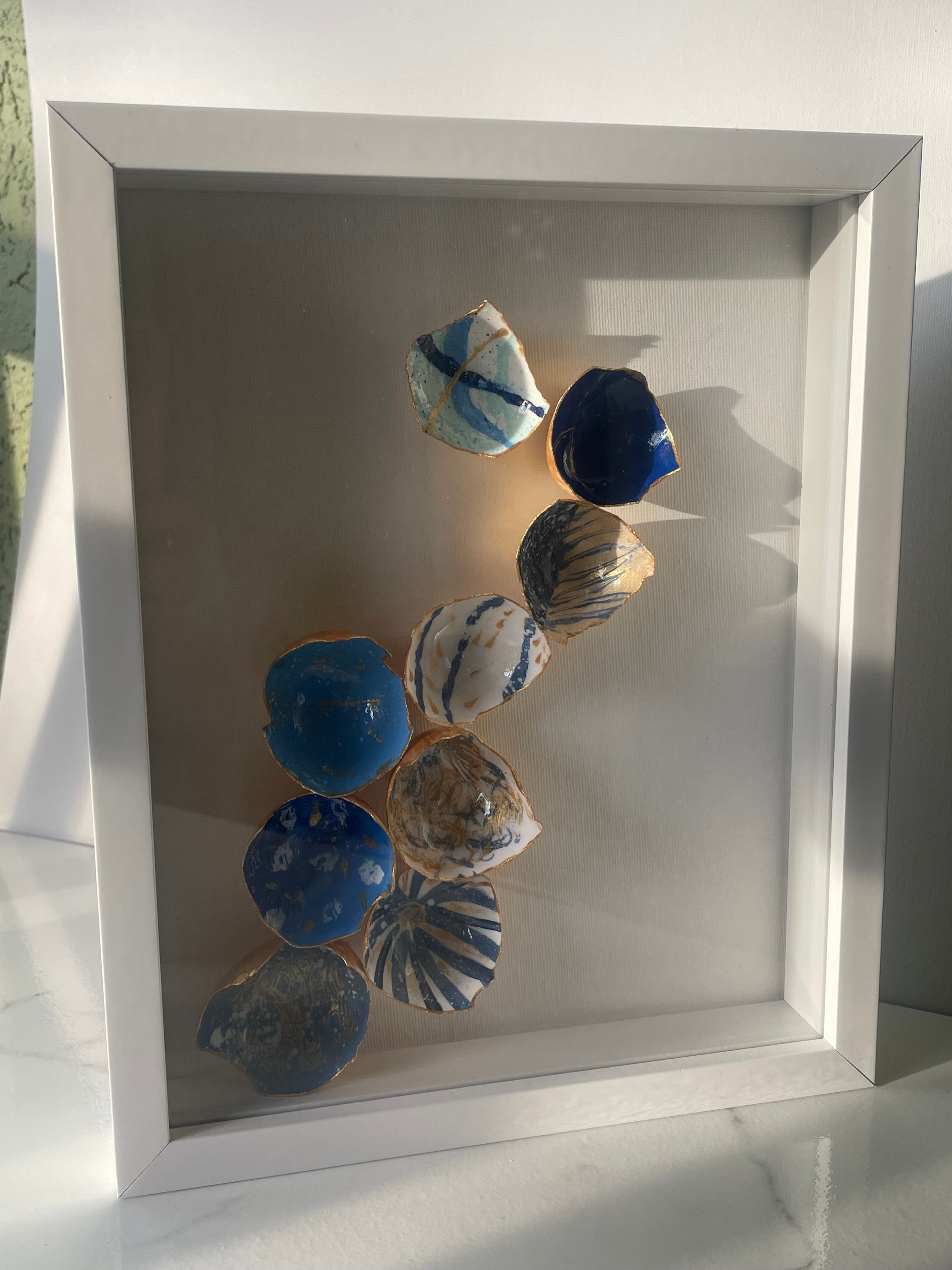 Side angle view of Coastal Cascade gilded eggshell kintsugi shadow box showing layered eggshells in blue and white with gold paint edges