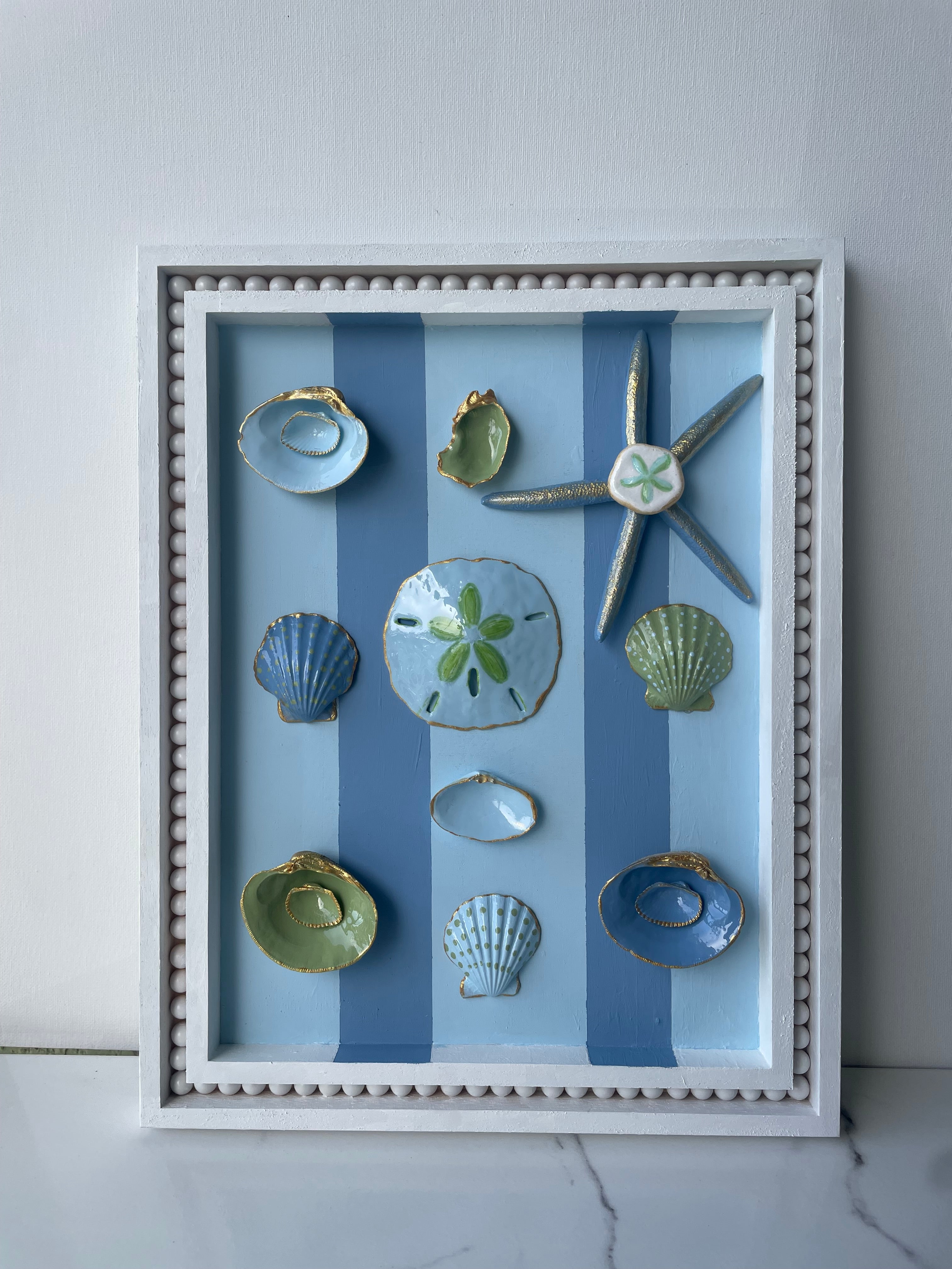 Original coastal wall art with oyster shells, starfish, and gold accents in an 11x14 wood frame". 